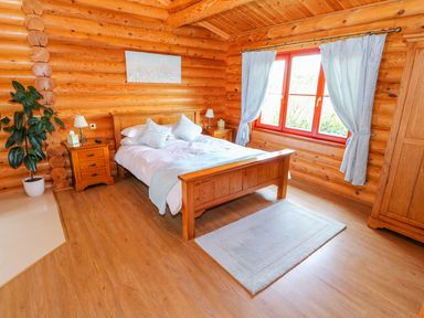 A bedroom with a wooden bed two bedside tables a plant and a window with curtains at Cedar Lodge in Greetham Rutland