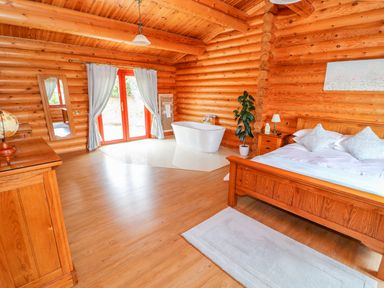 A bedroom with a wooden bed a chest of drawers a bathtub and a full-length mirror in a log cabin at Cedar Lodge in Greetham Rutland