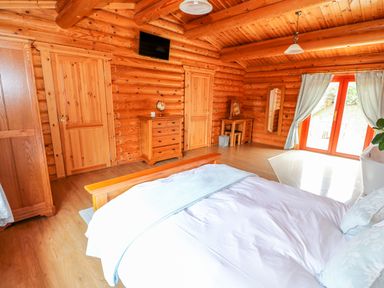 A bedroom with wooden walls a bed a dresser a small desk and large glass doors with curtains at Cedar Lodge in Greetham Rutland