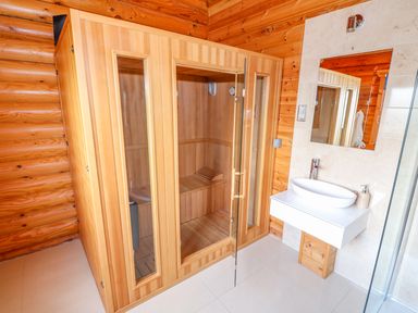 A wooden sauna cabin next to a white sink with a mirror in a bathroom at Cedar Lodge in Greetham Rutland