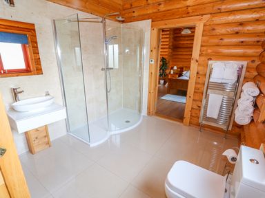 A bathroom with a shower area sink toilet towel rack and wooden walls at Cedar Lodge in Greetham Rutland