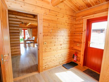 A wooden hallway with coat hooks and a fire extinguisher leading to a dining area in Cedar Lodge in Greetham Rutland