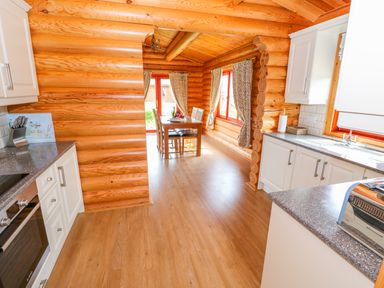 A kitchen with white cabinets a countertop and dining table with chairs in a wooden log cabin at Cedar Lodge in Greetham Rutland