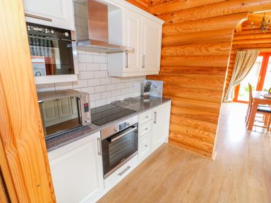 A kitchen with white cabinets a microwave a stove an oven and wooden walls at Cedar Lodge in Greetham Rutland