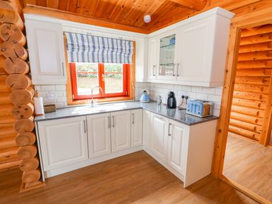 A kitchen with white cabinets a blue toaster kettle and coffee machine a window with striped blinds at Cedar Lodge in Greetham Rutland