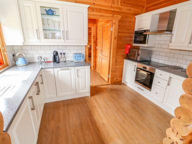 A kitchen with white cabinets wooden walls and floor with oven toaster and kettle at Cedar Lodge in Greetham Rutland