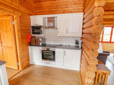 A kitchen area with white cabinets oven microwave and knife block in a wooden log cabin at Cedar Lodge in Greetham Rutland