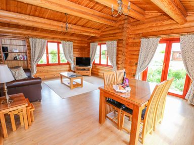 A living room with a dining table wooden chairs a couch coffee table television and bookshelves at Cedar Lodge in Greetham Rutland
