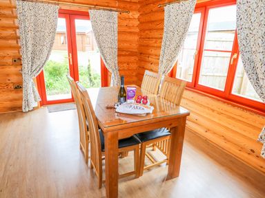 A dining area with a wooden table and six chairs inside a log cabin at Cedar Lodge in Greetham Rutland