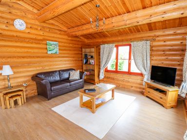 A living room with a leather sofa wooden coffee table TV on a stand and a bookshelf at Cedar Lodge in Greetham Rutland