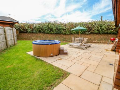 A backyard with a hot tub wooden lounge chairs table with umbrella and a barbecue grill at Cedar Lodge in Greetham Rutland
