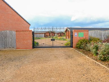 A gravel driveway leading to a black metal gate with brick pillars and wooden fencing surrounding the area at Cedar Lodge in Greetham Rutland