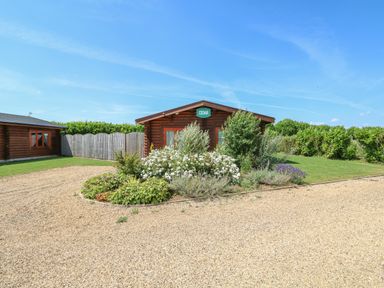A log cabin with a garden of shrubs and flowers in front at Cedar Lodge in Greetham Rutland