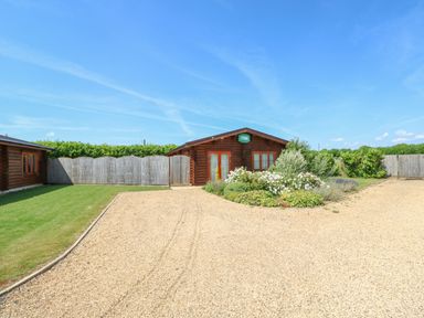 A gravel driveway leading to a wooden cabin with a garden and a fence in the background at Cedar Lodge in Greetham Rutland