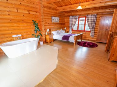 A bedroom with a wooden bed and a white bathtub on tiled floor at Beech Lodge Greetham Rutland