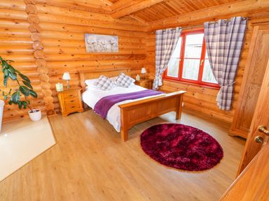 A bedroom with a wooden bed white bedding purple throw pillows and rug wooden furniture and plaid curtains at Beech Lodge Greetham Rutland