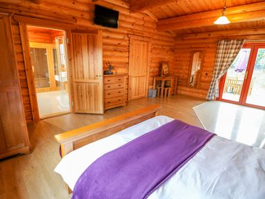 A bedroom with wooden furniture and walls a bed with a purple blanket a dresser a vanity table and glass doors at Beech Lodge in Greetham Rutland