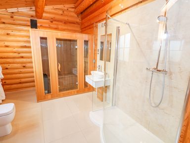 A bathroom with a glass shower, wooden sauna, white sink, and toilet at Beech Lodge in Greetham Rutland