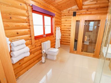 A bathroom with wooden walls a toilet a sauna towels and bathrobes at Beech Lodge in Greetham Rutland