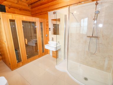 A bathroom with a wooden sauna unit a wall-mounted sink and a glass shower enclosure at Beech Lodge in Greetham Rutland