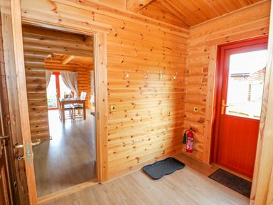 A wooden hallway with coat hooks fire extinguisher and red door opening to a dining area with table and chairs at Beech Lodge in Greetham Rutland