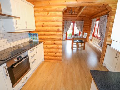 A kitchen with white cabinets and black countertops opening to a dining area with a wooden table and chairs in a log cabin at Beech Lodge in Greetham Rutland