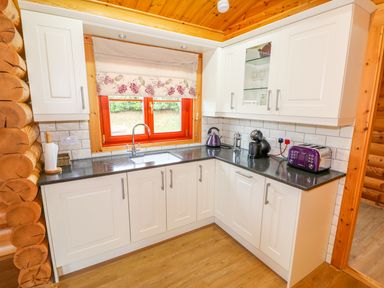 A kitchen with white cabinets a black countertop a window above the sink and small appliances at Beech Lodge Greetham Rutland