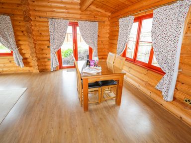 A dining area with a wooden table and four chairs in a log cabin with floral curtains at Beech Lodge in Greetham Rutland
