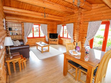 A wooden living room with a brown leather sofa a coffee table a TV on a wooden stand and a dining table with chairs at Beech Lodge in Greetham Rutland