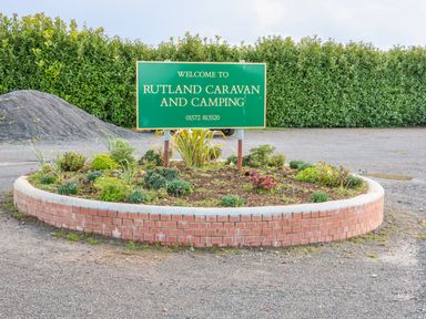 Welcome sign for rutland caravan and camping in a planted circular brick flower bed in a gravel parking area