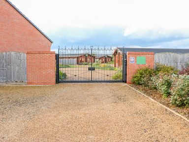 A gravel driveway with a black iron gate and brick pillars leading to wooden lodges at Beech Lodge in Greetham Rutland