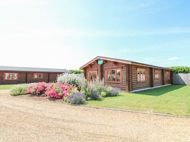 A wooden cabin with flowers and a gravel pathway at Beech Lodge in Greetham Rutland