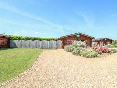 A gravel driveway leading to wooden lodges with plants and grass at Beech Lodge in Greetham Rutland