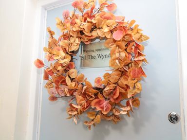 A door with an autumn leaf wreath and a sign reading Wynding Apartment at Wynding Apartment in Amble-By-The-Sea