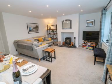 A living room with a gray sofa and yellow cushions a wood burning stove and a TV at Wynding Apartment in Amble-By-The-Sea