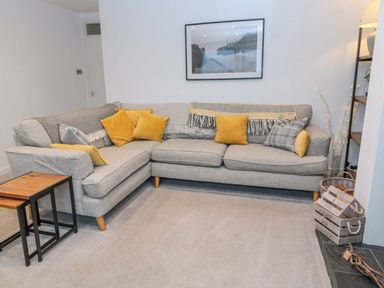 A grey corner sofa with yellow and grey cushions and a framed picture above at Wynding Apartment in Amble-By-The-Sea