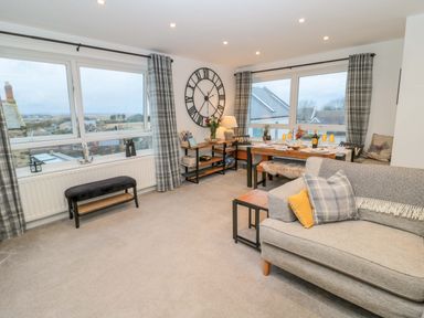 A living room with a sofa a dining table with place settings and large windows with curtains at Wynding Apartment in Amble-By-The-Sea