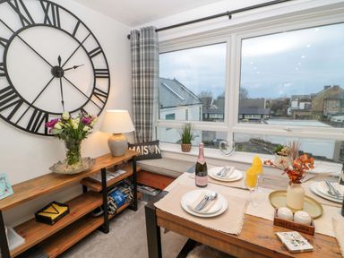 A dining area with a wooden table set for two near a large window and a corner bench at Wynding Apartment in Amble-By-The-Sea