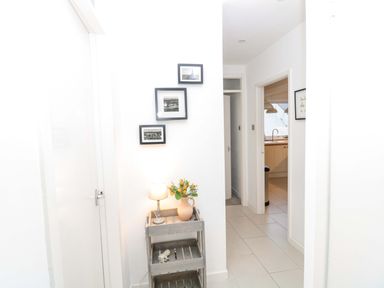 A hallway with a small wooden shelf holding a lamp and a vase with flowers and three framed photos on the wall at Wynding Apartment in Amble-By-The-Sea