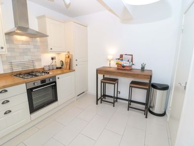 A kitchen with white cabinets a wooden countertop a stove oven and a small table with stools and a lamp at Wynding Apartment in Amble-By-The-Sea