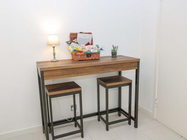 A wooden table with two stools a lamp a wicker basket with snacks and a small plant at Wynding Apartment in Amble-By-The-Sea