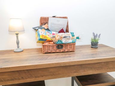 A wooden table with a lamp a wicker basket containing groceries and a small plant pot at Wynding Apartment in Amble-By-The-Sea