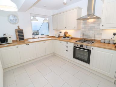 A kitchen with white cabinets wooden countertops a sink microwave oven and stove at Wynding Apartment in Amble-By-The-Sea