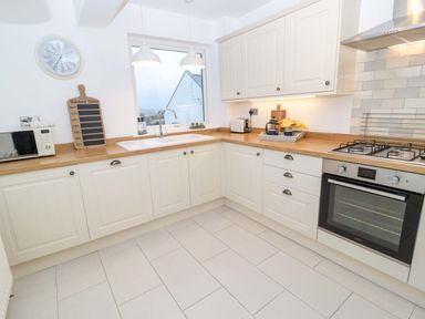 A kitchen with white cabinets a wooden countertop a gas stove and oven a microwave and a sink at Wynding Apartment in Amble-By-The-Sea