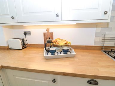 A kitchen countertop with a toaster a tray with cups a French press and toast at Wynding Apartment in Amble-By-The-Sea