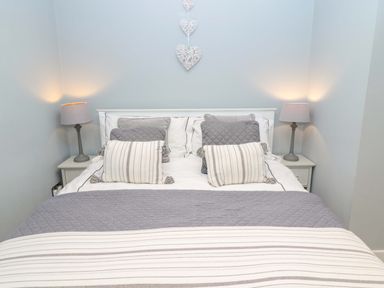 A bedroom with a bed with striped and quilted pillows and lamps on bedside tables at Wynding Apartment in Amble-By-The-Sea