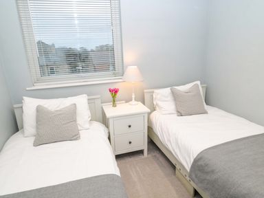 A bedroom with two single beds a nightstand a lamp and flowers at Wynding Apartment in Amble-By-The-Sea