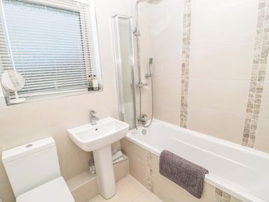 A bathroom with a bathtub a sink a toilet a window with blinds and a mirror at Wynding Apartment in Amble-By-The-Sea