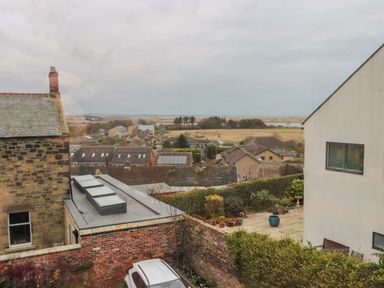 A view of residential houses with a garden and parked car in the foreground at Wynding Apartment in Amble-By-The-Sea