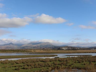 A marshland area with grassy patches and water bodies with mountains in the background at Wynding Apartment in Amble-By-The-Sea